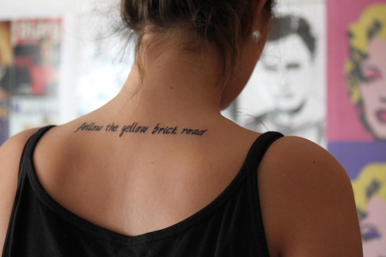 Follow The Yellow Brick Road Quote Tattoo On Girl Back Neck