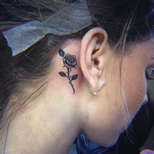 Black Ink Rose Tattoo On Girl Right Behind The Ear