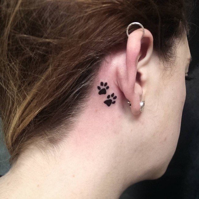 Black Paw Prints Tattoo On Girl Right Behind The Ear