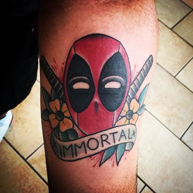 Deadpool Head With Flowers And Banner Tattoo Design