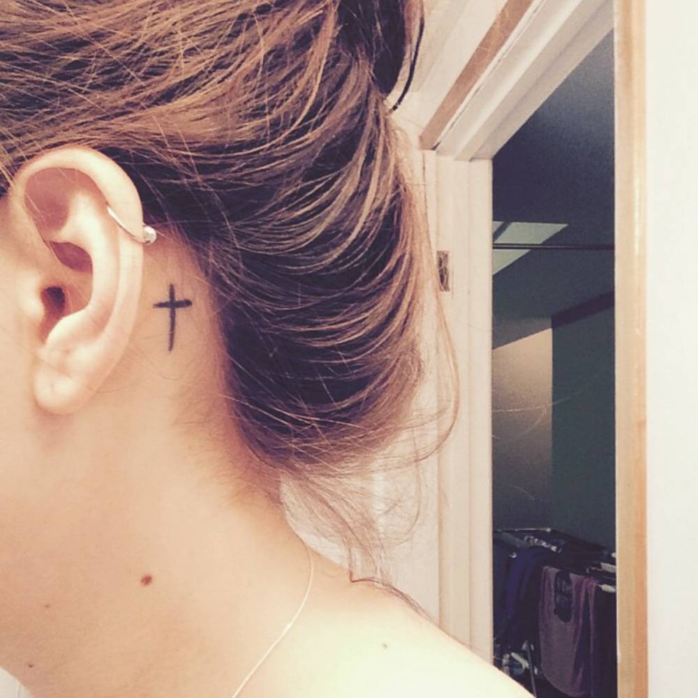 Simple Black Cross Tattoo On Girl Left Behind The Ear