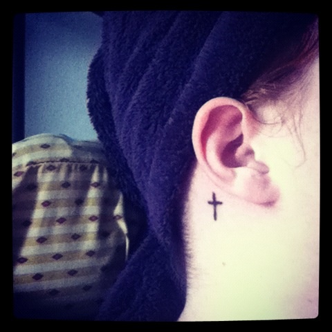 Simple Black Cross Tattoo On Right Behind The Ear