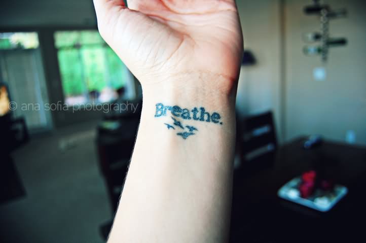 Simple Breathe Lettering With Flying Birds Tattoo On Left Wrist