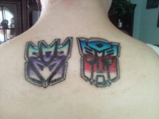 Colorful Two Transformer Logo Tattoo On Upper Back By Jennifer