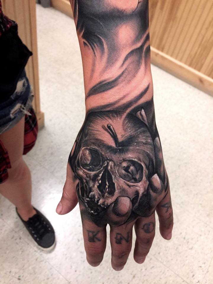 Grey Ink Apple Skull Tattoo On Left Hand by Carl Grace