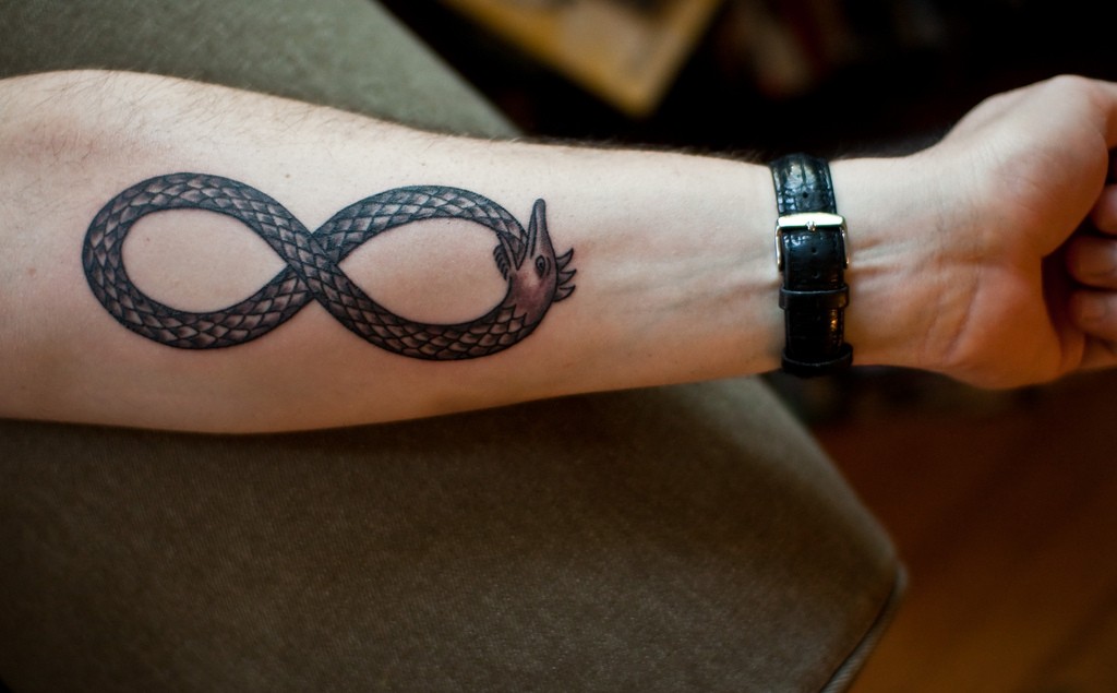 Grey Ink Infinity Ouroboros Tattoo On Forearm