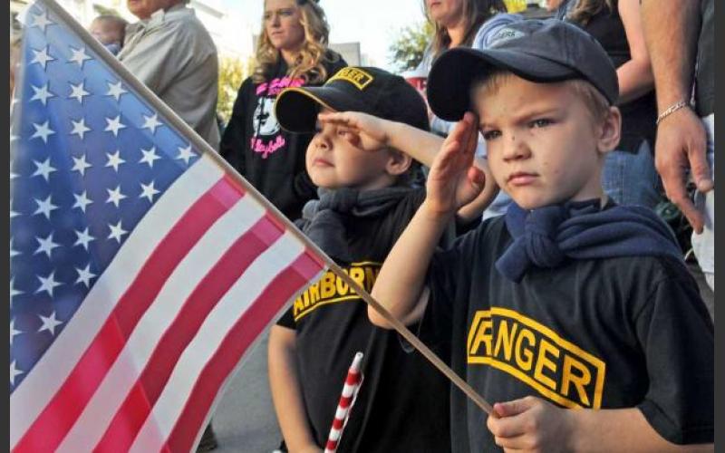 Kid With American Flag In Hand Saluting During Veterans Day Parade