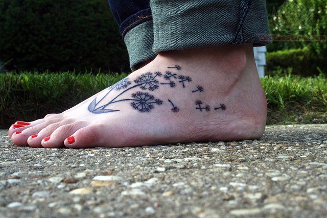 Dandelion Blowing From Puff In Deep Black Ink Tattoo On Foot