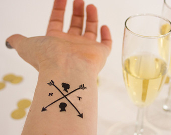Two Crossed Arrows With Tiny Men And Women Faces Tattoos On Wrist