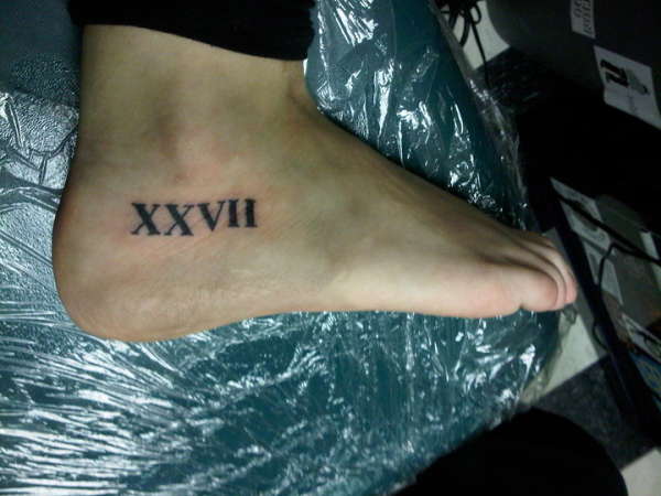 Black Color Roman Numeral Tattoo On Foot
