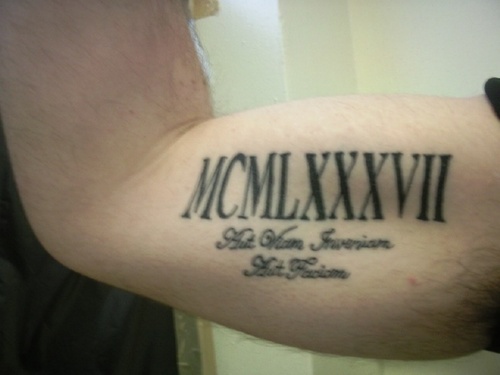 Black Ink Roman Numerals With Lettering Tattoo On Bicep