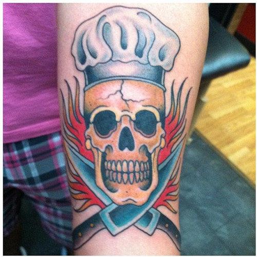 Chef Skull With Crossed Knives And Flames Tattoo On Forearm
