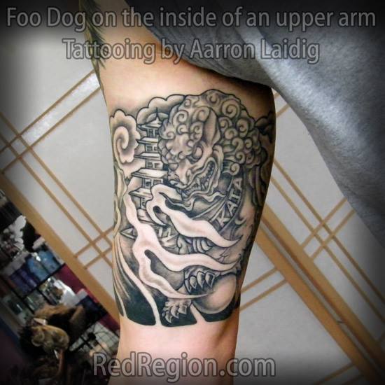 Black And Grey Ink Foo Dog With Temple Tattoo On Bicep