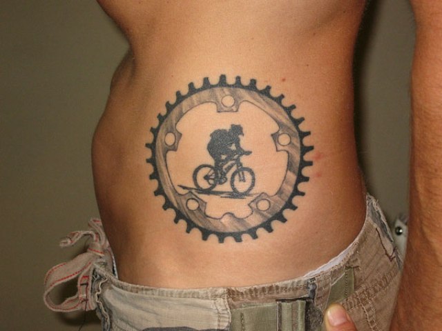 Black Color Person Riding Cycle In Wheel Tattoo On Side Rib
