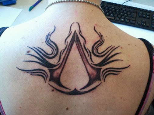 Black And Grey Assassins Creed Tattoo On Upper Back
