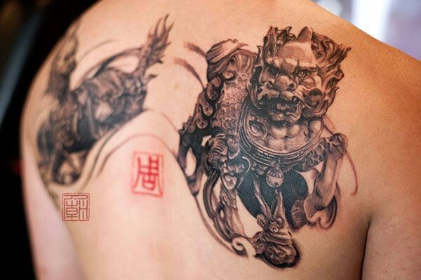 Black And Grey Colored Chinese Foo Dogs With Symbol Tattoo On Upper Back