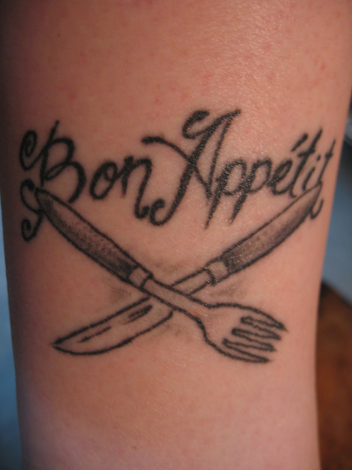 Grey Crossed Knife And Fork With Bon Appetit Words Tattoo