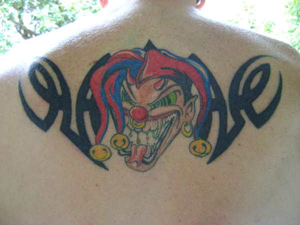 Colorful Evil Jester Head With Tribal Design Tattoo On Upper Back