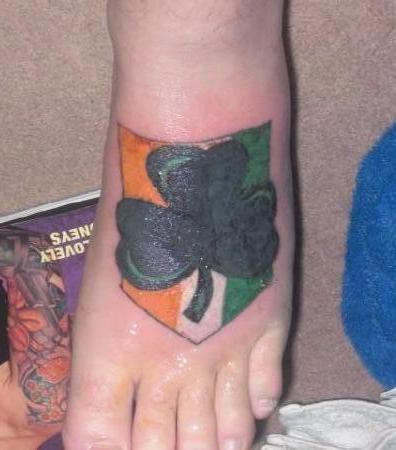 Nice Dark Green Shamrock With Ireland Flag In Background Tattoo On Foot