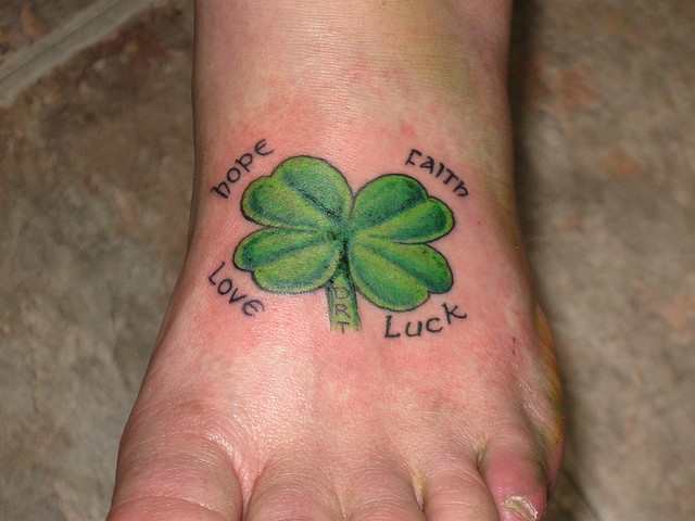 Nice Lettering With Four Leaf Shamrock Tattoo On Foot