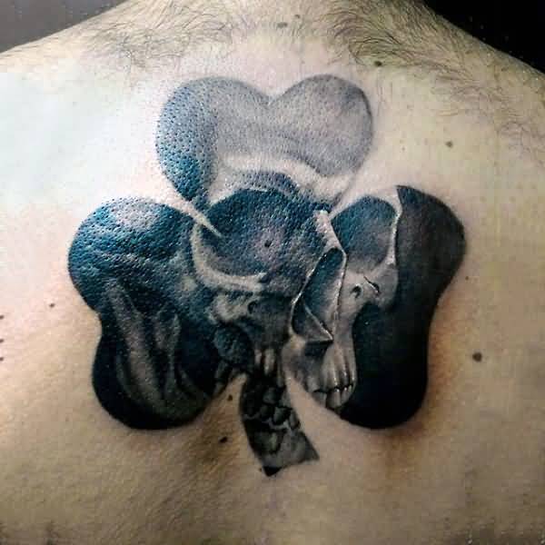 Superb Black Skull In Shamrock Leaf Tattoo On Upper Back