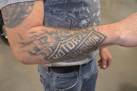 Flaming Grey And Black Harley Bike Logo Tattoo On Forearm