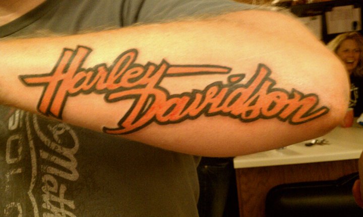 Orange Harley Davidson Word Tattoo On Forearm