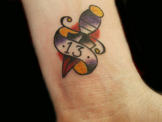 Tiny Dagger And Banner Tattoo On Wrist