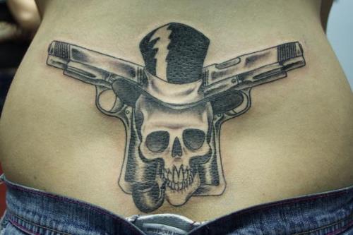 Skull Wearing Hat And Weapons Tattoo On Lower Back