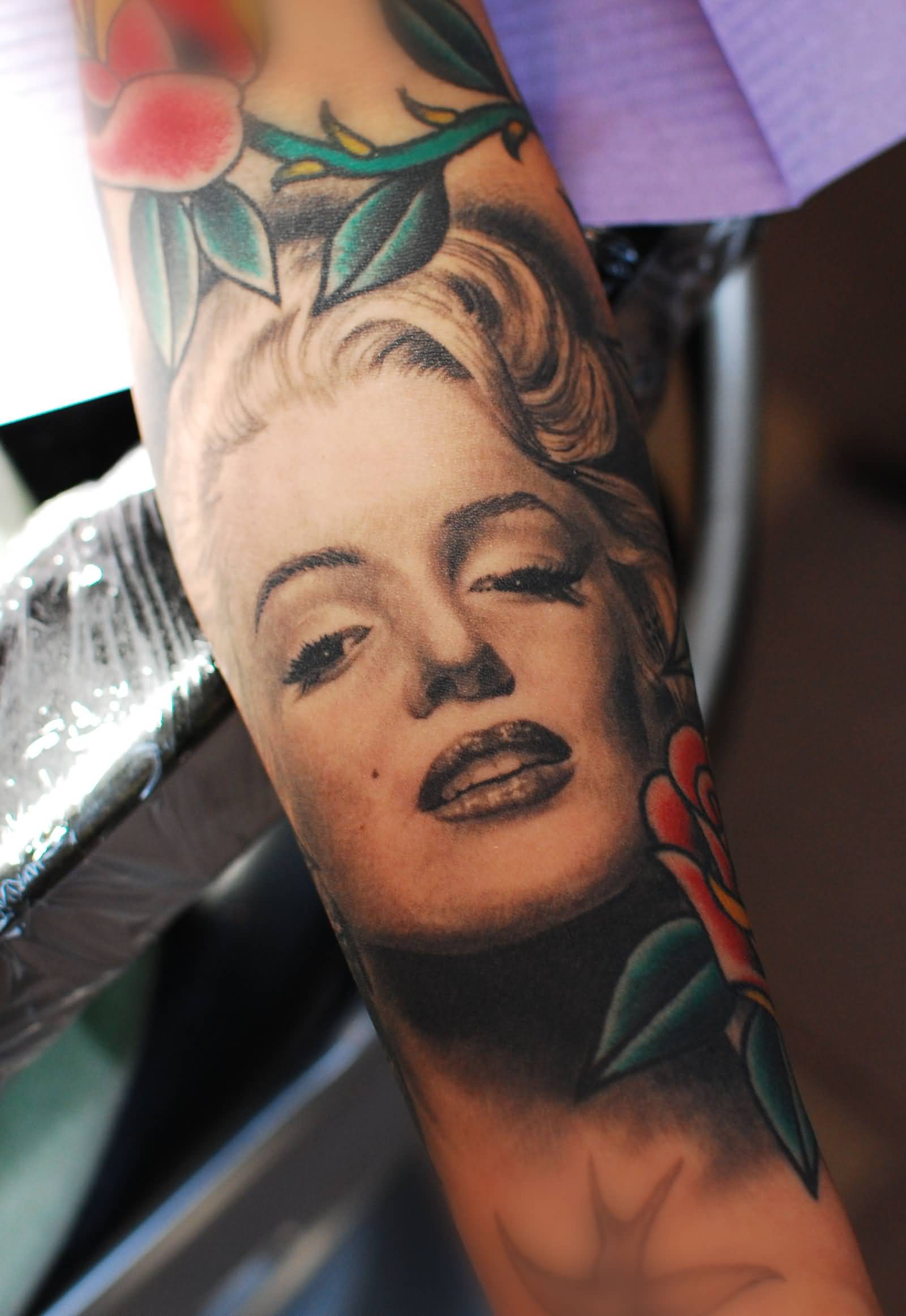 Marilyn Monroe Portrait With Traditional Flowers Tattoo On Arm