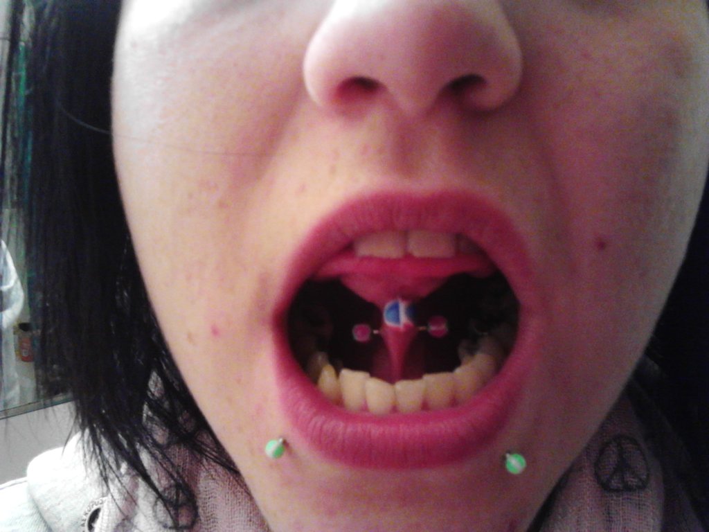 Lower Lip Piercings With Green Studs And Tongue Frenulum Piercing.