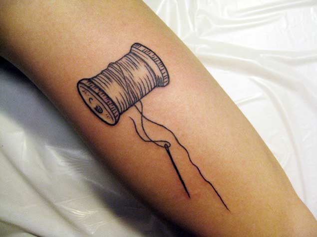 Grey Sewing Spool And Needle Tattoo On Arm