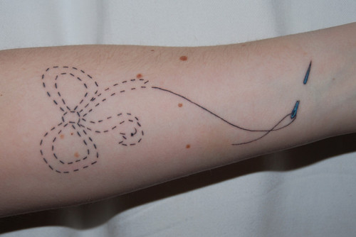 Simple Sewing Ribbon Tattoo On Forearm
