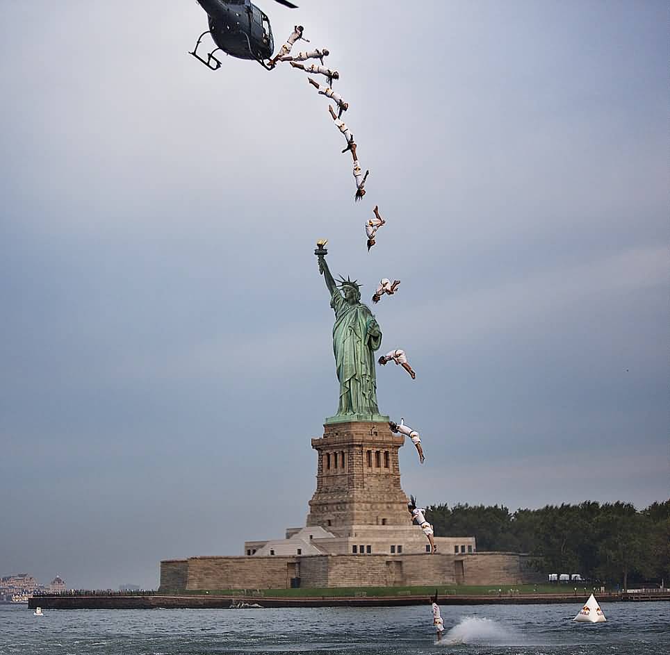 World Champion Cliff Diver Completes A Flying Back Diver In Front Of Statue Of Liberty