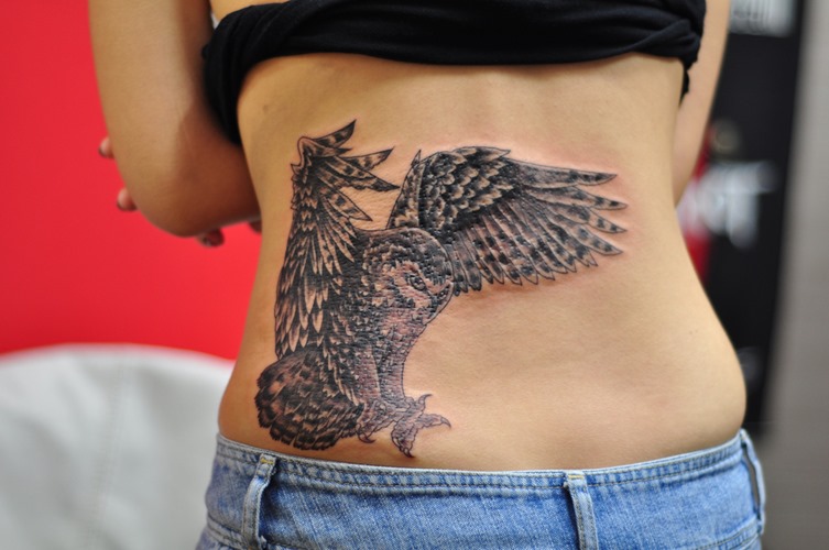 Black And Grey Flying Owl Tattoo On Girl Lower Back