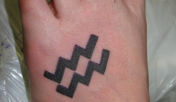 Black Ink Aquarius Zodiac Sign Tattoo On Left Foot