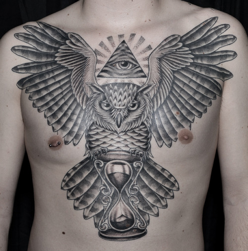 Black Ink Flying Owl With Hourglass And Illuminati Eye Tattoo On Man Chest