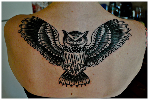 Attractive Black Ink Flying Owl Tattoo On Upper Back