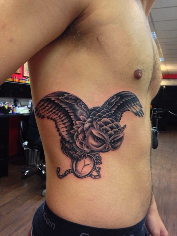 Black Ink Flying Owl With Clock Tattoo On Man Right Side Rib By Piers Lee