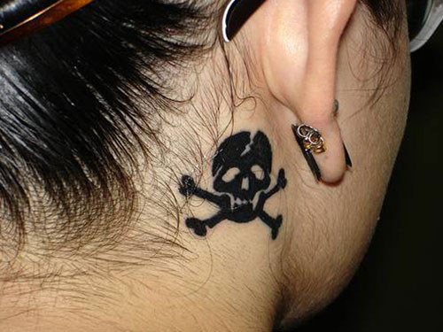 Black Ink Pirate Skull With Crossbone Tattoo On Girl Right Behind The Ear