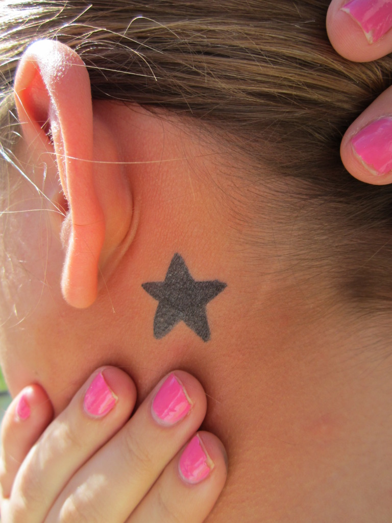 Girl Showing Her Black Star Tattoo Behind Ear