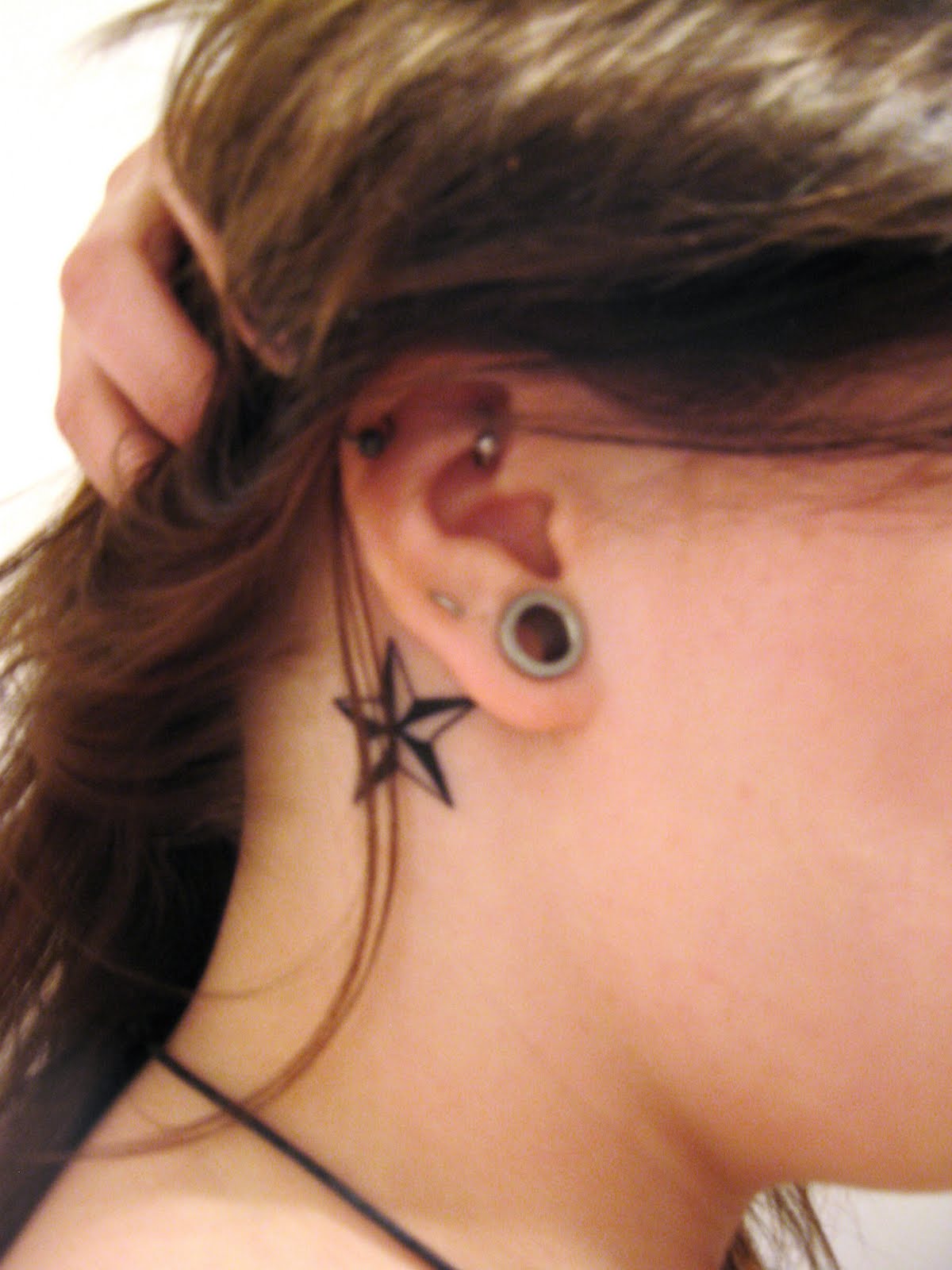 Girl Showing Her Nautical Star Tattoo Behind The Ear