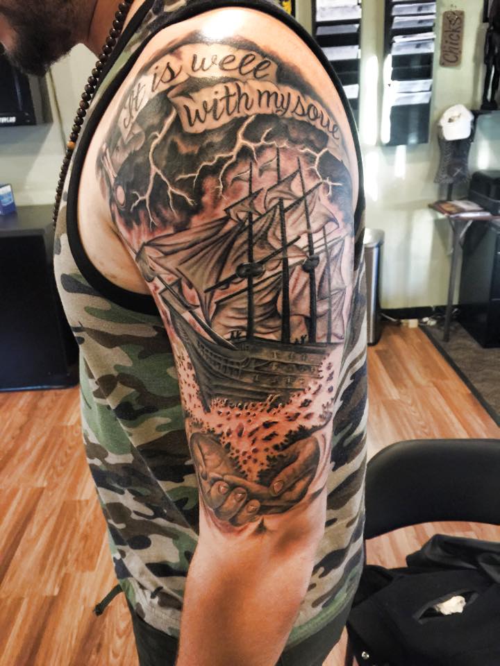 Black Ink Ship With Banner Tattoo On Man Left Half Sleeve