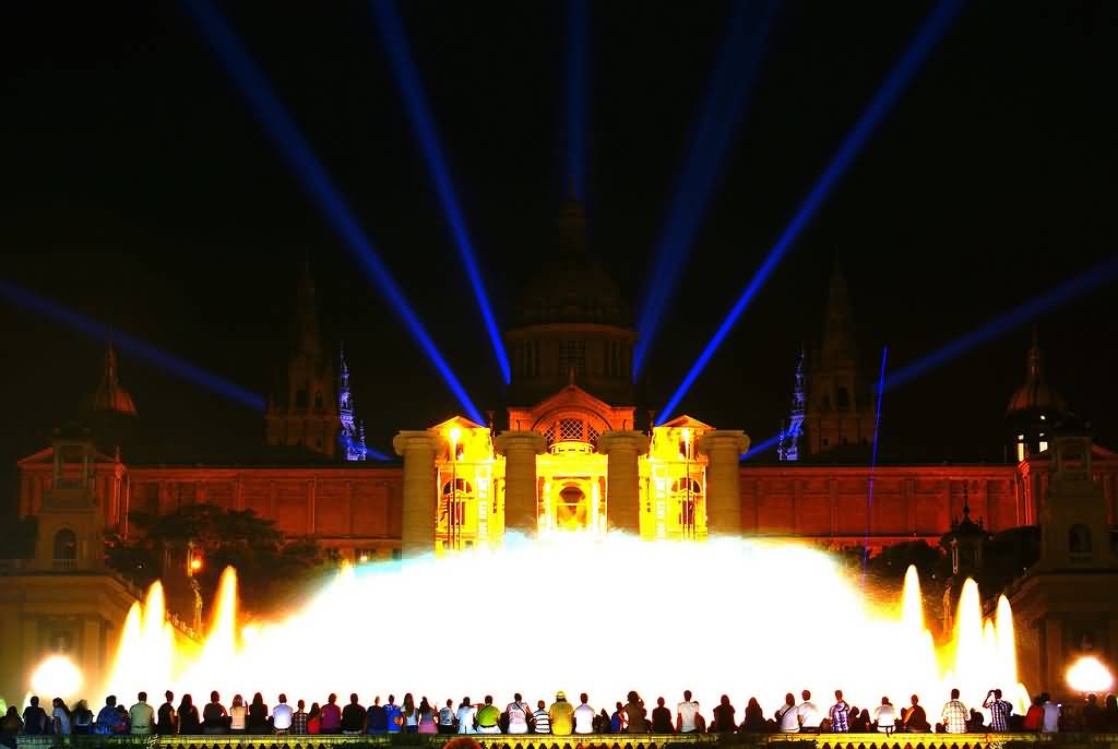 Tourists Enjoying The Fountain Show In Front Of Palau Nacional At Night