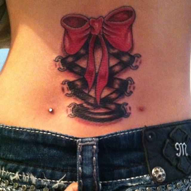 Black Ink Corset With Pink Bow Tattoo On Lower Back