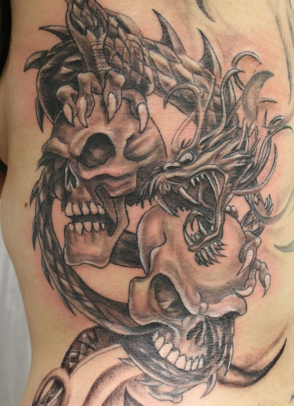 Black Ink Dragon Wrap Around Skulls Tattoo On Left Side Rib