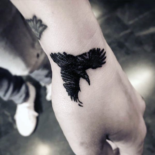 Small Black Flying Crow Tattoo On Left Hand