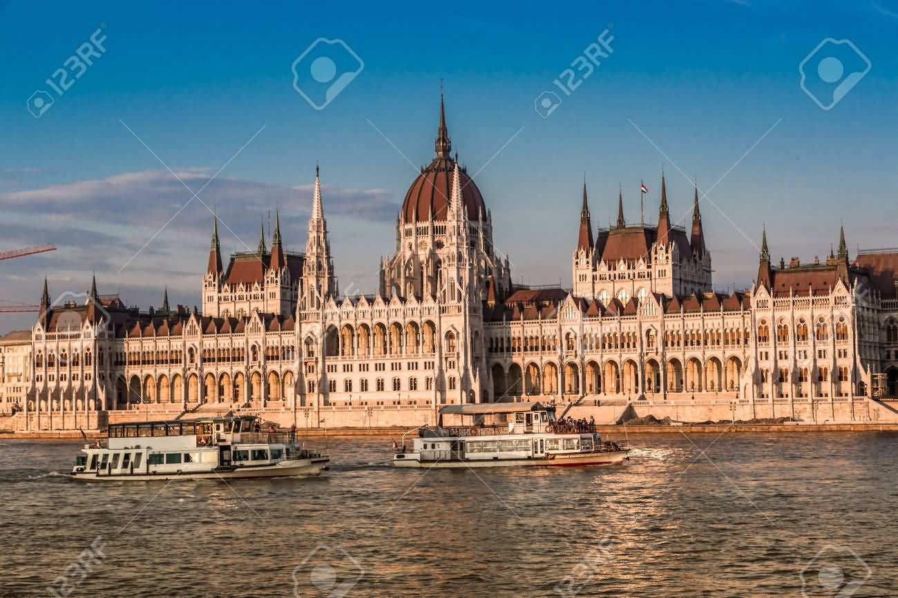 Two Boats In Danube River Passing Near From The Hungarian Parliament Building