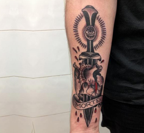 Black Ink Dagger In Real Heart With Banner Tattoo On Right Forearm