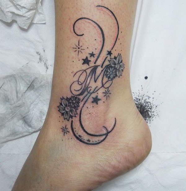 Black Ink Flowers With M Letter Tattoo On Left Ankle
